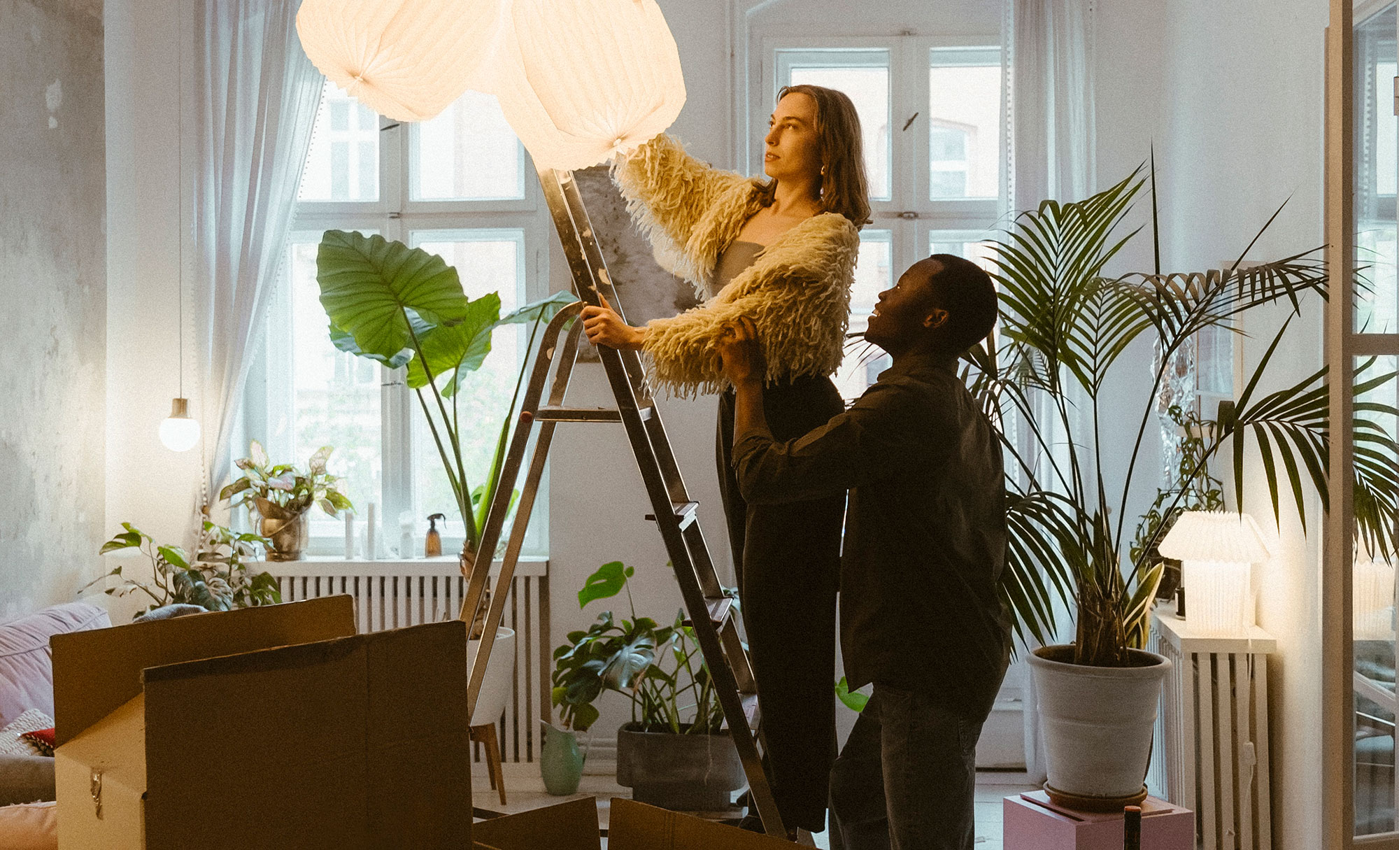 A couple hanging a ceiling lamp in their new apartment